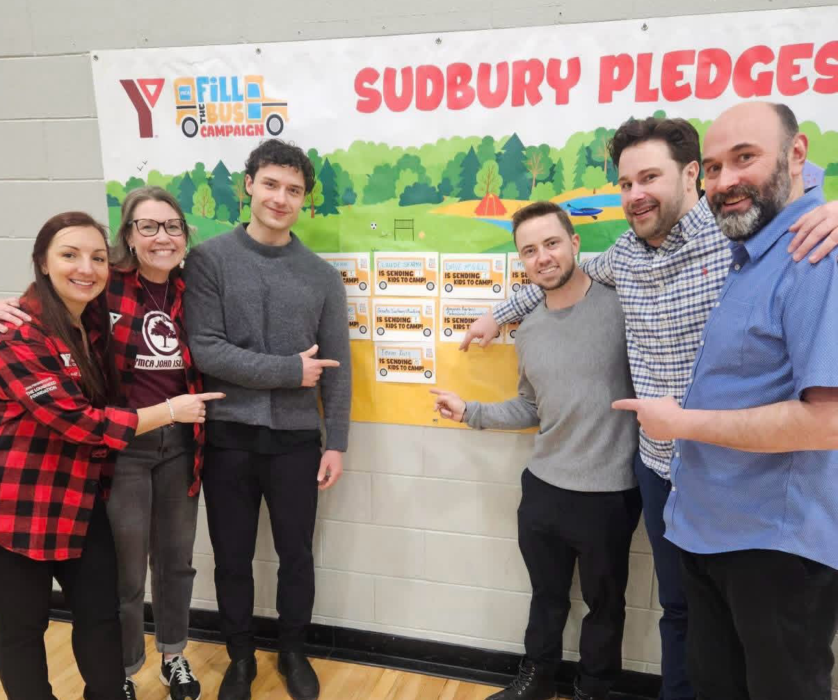 Team King members standing beside the YMCA Fill the Bus Sudbury pledge board after raising $4,100 to send 15 kids to John Island Camp in 2026.